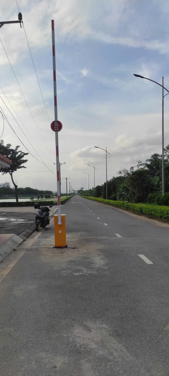 Thanh chắn barie tự động màu vàng trắng giữa đường nhựa hai làn, cạnh đó là xe máy dựng bên lề